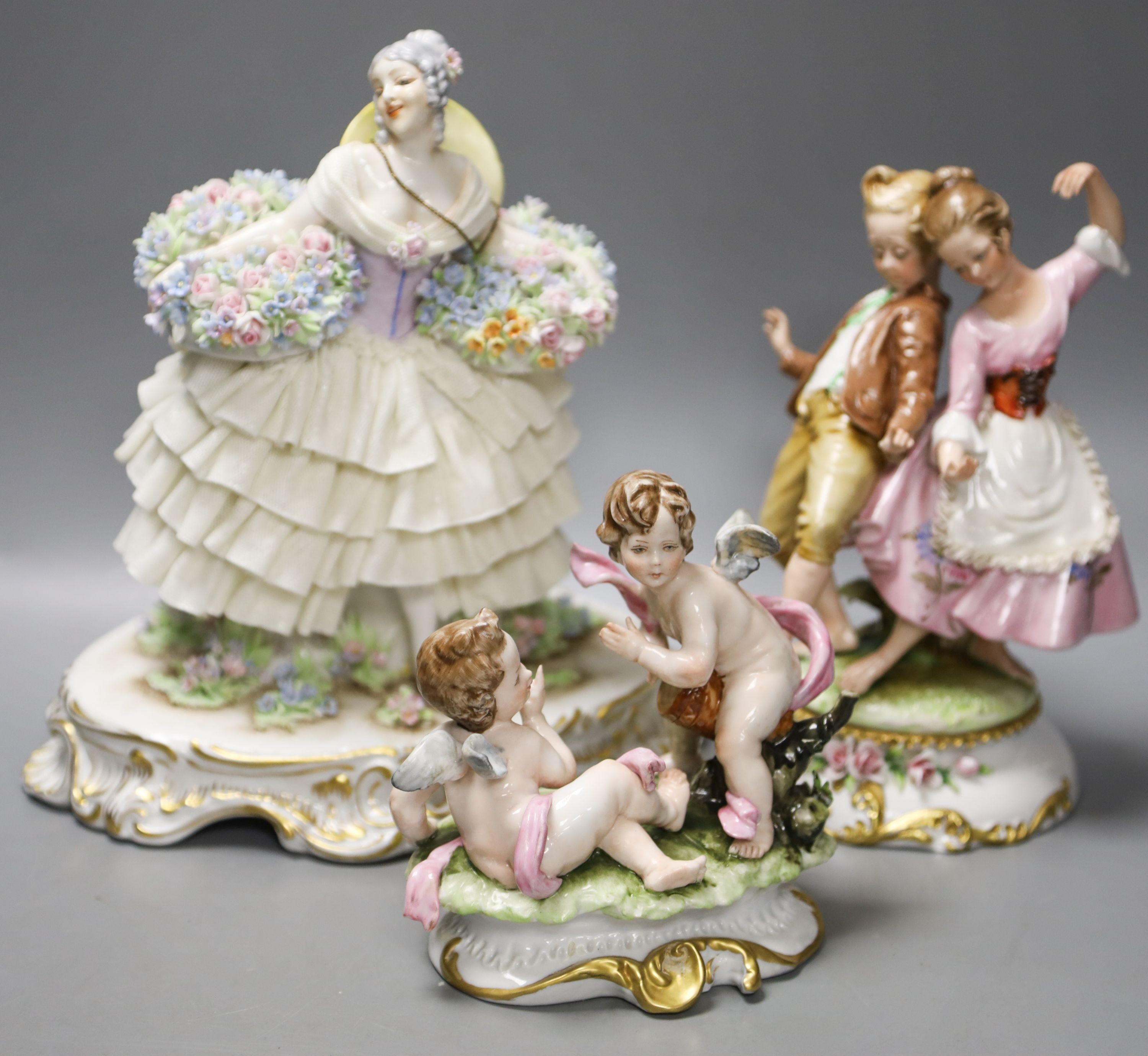 A Luigi Fabris porcelain figure of a lady wearing a crinoline dress, holding baskets of flowers, and two other figural groups (3)